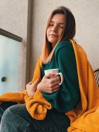 Young woman holding coffee cup with eyes closed sitting at home
