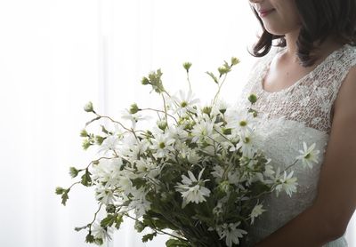 Midsection of woman holding white flowers while standing at home