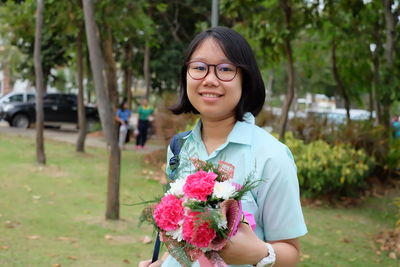Portrait of smiling young woman with bouquet standing in park