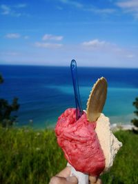 Close-up of hand holding ice cream against sea