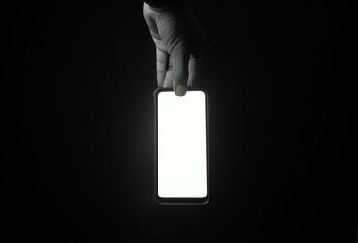 Close-up of hand holding light bulb against black background