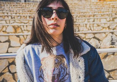 Portrait of young woman wearing sunglasses standing against brick wall