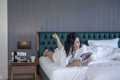 Woman reading magazine while lying on bed at home