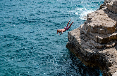 Young man cliff dive jumping into sea.