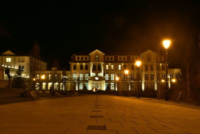 Illuminated street amidst buildings against sky at night