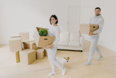 Smiling couple holding box standing on floor with dog