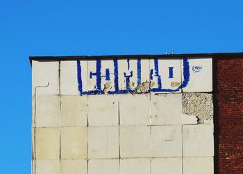 Low angle view of text on wall against clear blue sky