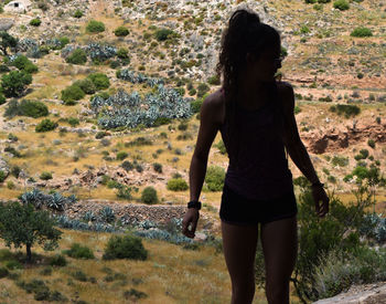 Rear view of young woman standing on rock against trees