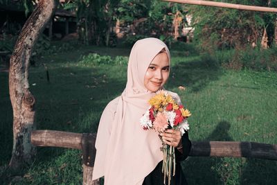 Portrait of beautiful woman holding flowers while standing by railing