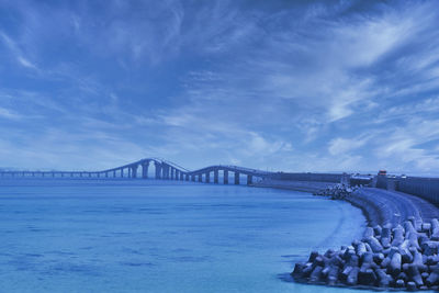 Bridge over calm sea against cloudy sky