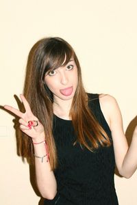 Portrait of young woman gesturing while sticking out tongue against wall