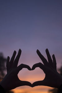 Silhouette of hand making heart shape against sky during sunset
