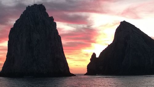 Silhouette of rock in sea against cloudy sky