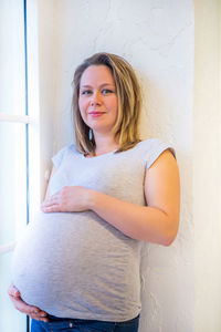 Portrait of pregnant woman standing against window at home