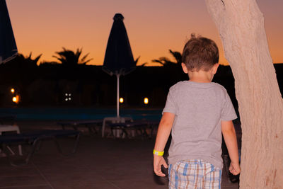 Rear view of boy standing against sky during sunset