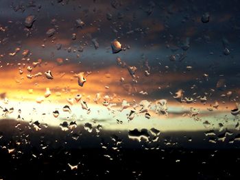 Water drops on glass window against sky during sunset