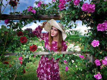 Portrait of young woman with hat weraring a pink dress in a garden of roses