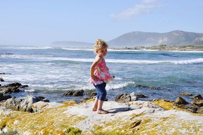 Full length of girl standing on rock at beach against sky