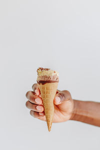 Cropped hand of man holding ice cream cone against gray background