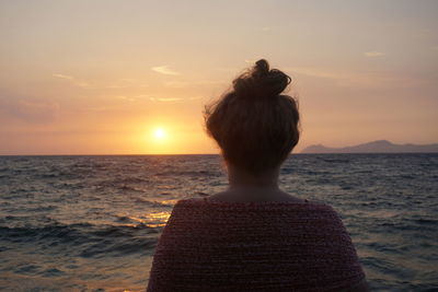 Rear view of woman standing at beach during sunset