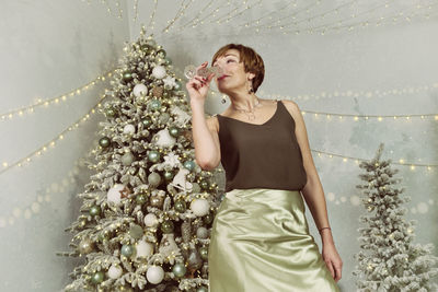 An adult woman drinks champagne next to a christmas tree on new year's eve