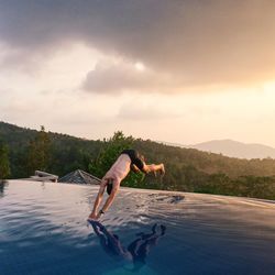 Shirtless man diving into swimming pool against sky during sunset