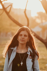 Portrait of young woman standing against tree