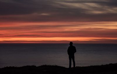 Rear view of silhouette man standing at beach during sunset