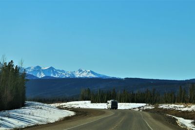 Road by snowcapped mountains against clear sky