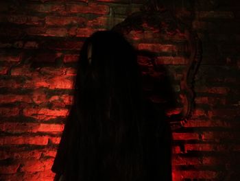 Rear view of woman standing against brick wall