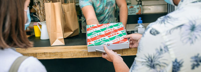 Owner giving pizza take away to customers at restaurant