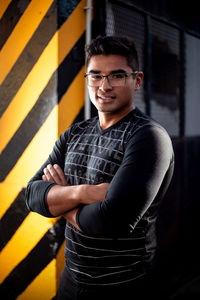 Portrait of young man with arms crossed standing against wall