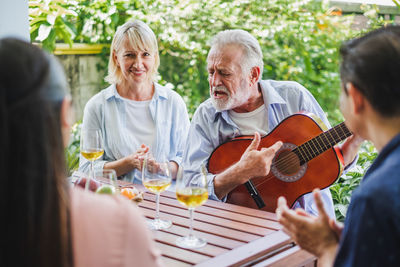 Smiling senior man playing guitar while sitting with friends at table