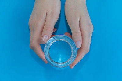 Cropped hands holding drinking glass over blue background