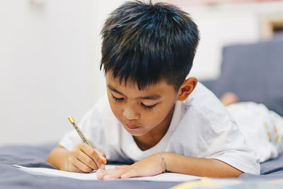 Cute boy writing in book at home