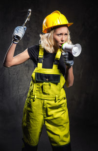 Female construction worker shouting on megaphone while standing against wall