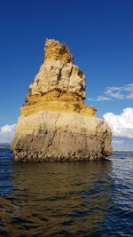 Rock formation by sea against blue sky