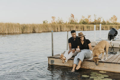 Smiling couple sitting with dog on pier