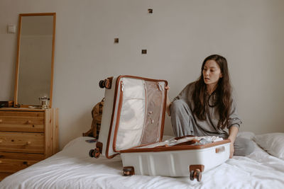 Young woman with open suitcase on the bed at home
