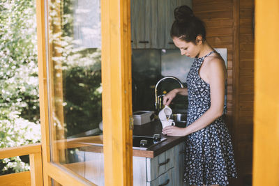 Young woman in summer dress pouring coffee in the kitchen