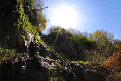Low angle view of waterfall against sky on sunny day