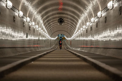 Rear view of man riding bicycle in illuminated tunnel