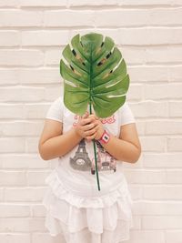 Girl holding leaf while standing against wall