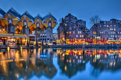 Illuminated buildings by lake against sky at night