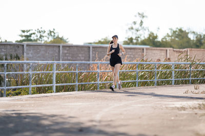 Full length of young woman running on footpath