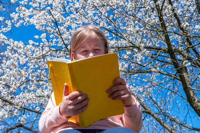 Low angle view of woman holding book against sky