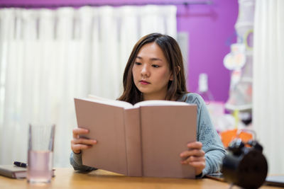 Young woman looking away while sitting on book at home