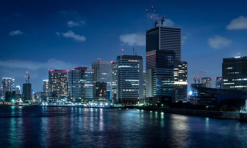 Illuminated buildings by river against sky in city