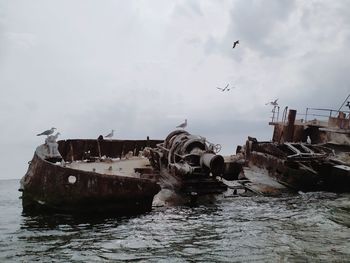 Seagulls flying over ship wreck on sea against sky