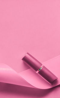 Cropped hand holding red lipstick against pink background